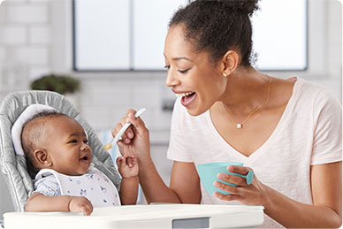 A smiling woman feeding a baby