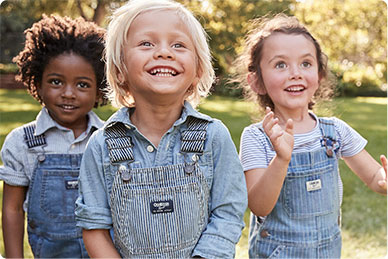 Three smiling children in OshKosh overalls
